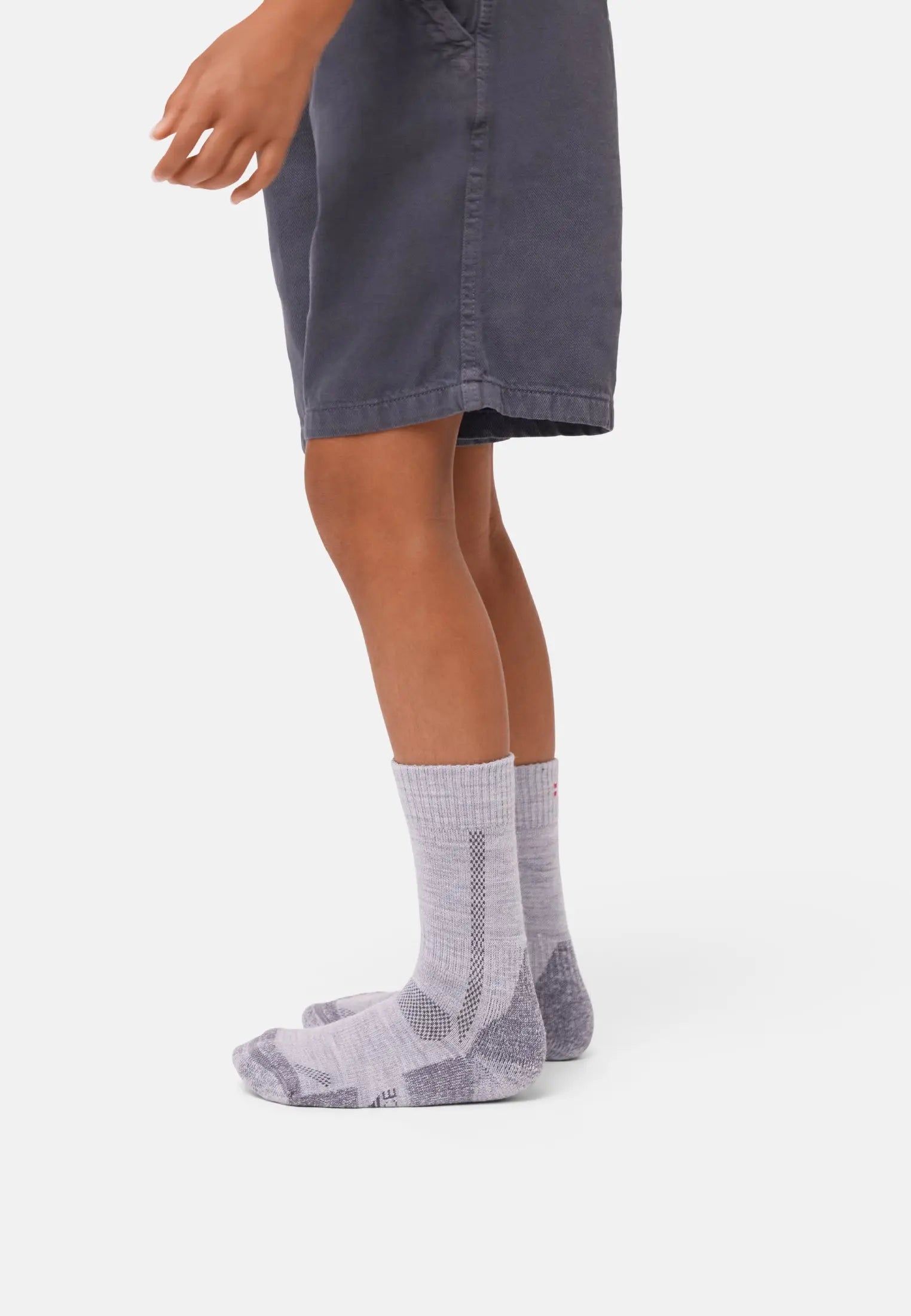 Child wearing gray merino wool hiking socks, standing on a white background, wearing shorts.