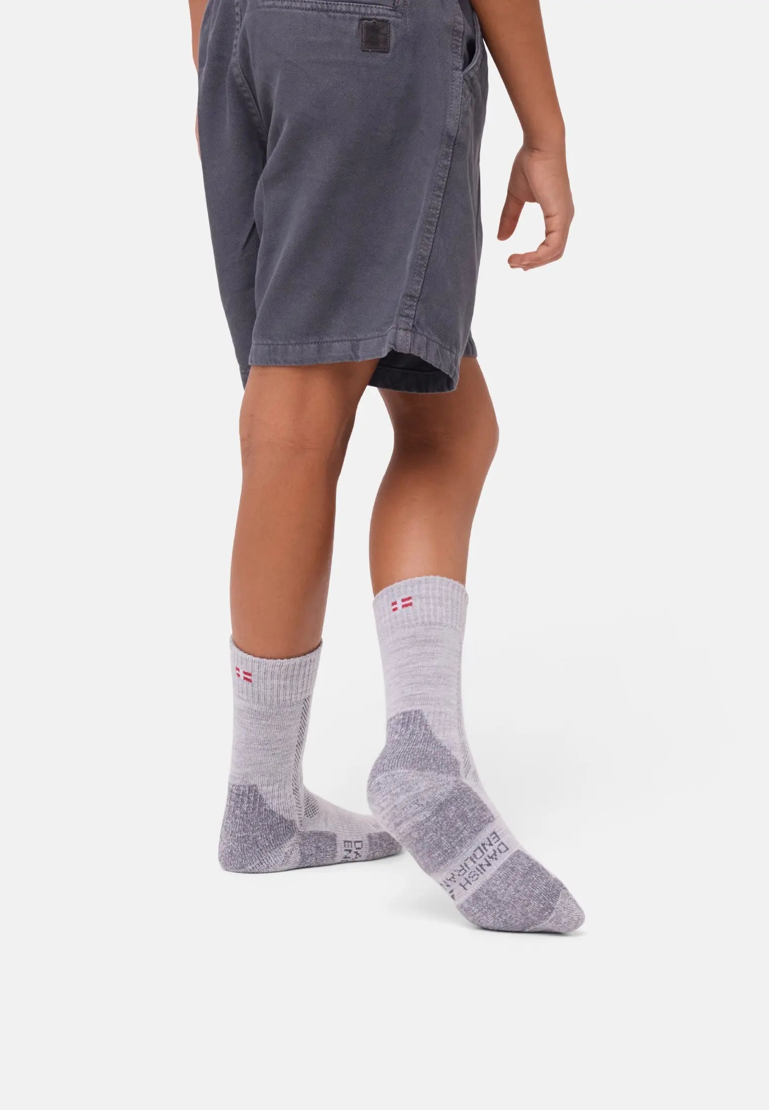 Child wearing gray shorts and light gray merino wool socks with red detail on white background.