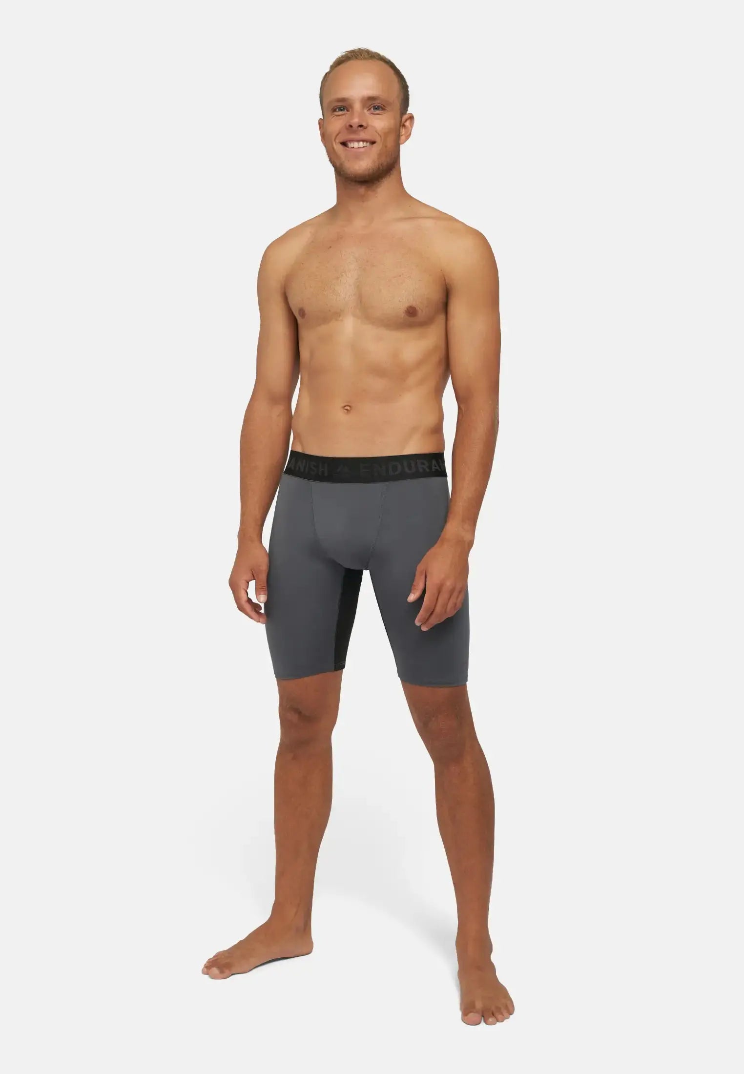 Man wearing gray compression shorts, standing barefoot, plain background.