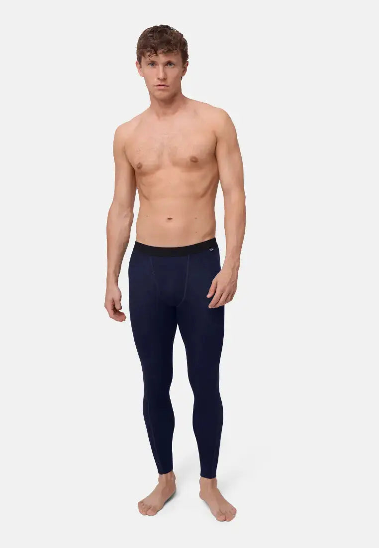 Man wearing dark blue merino wool base layer pants, standing against a light background.