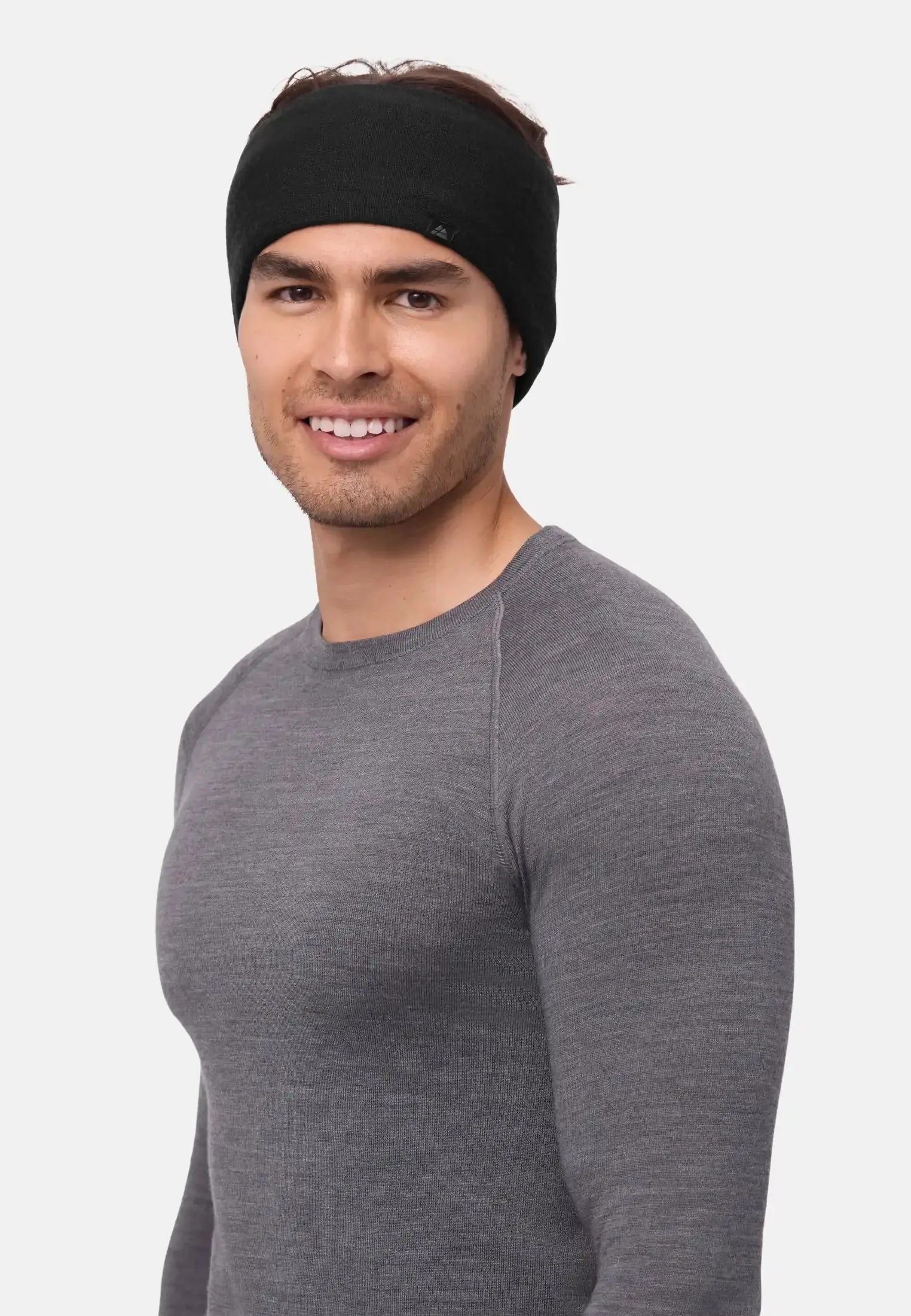 Person wearing a black merino headband with polar fleece, smiling, in a grey sweater against a plain backdrop.