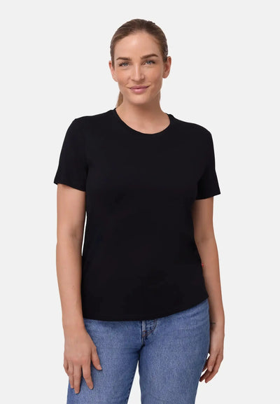 Woman wearing a black Merino T-shirt and blue jeans, smiling, against a white backdrop.