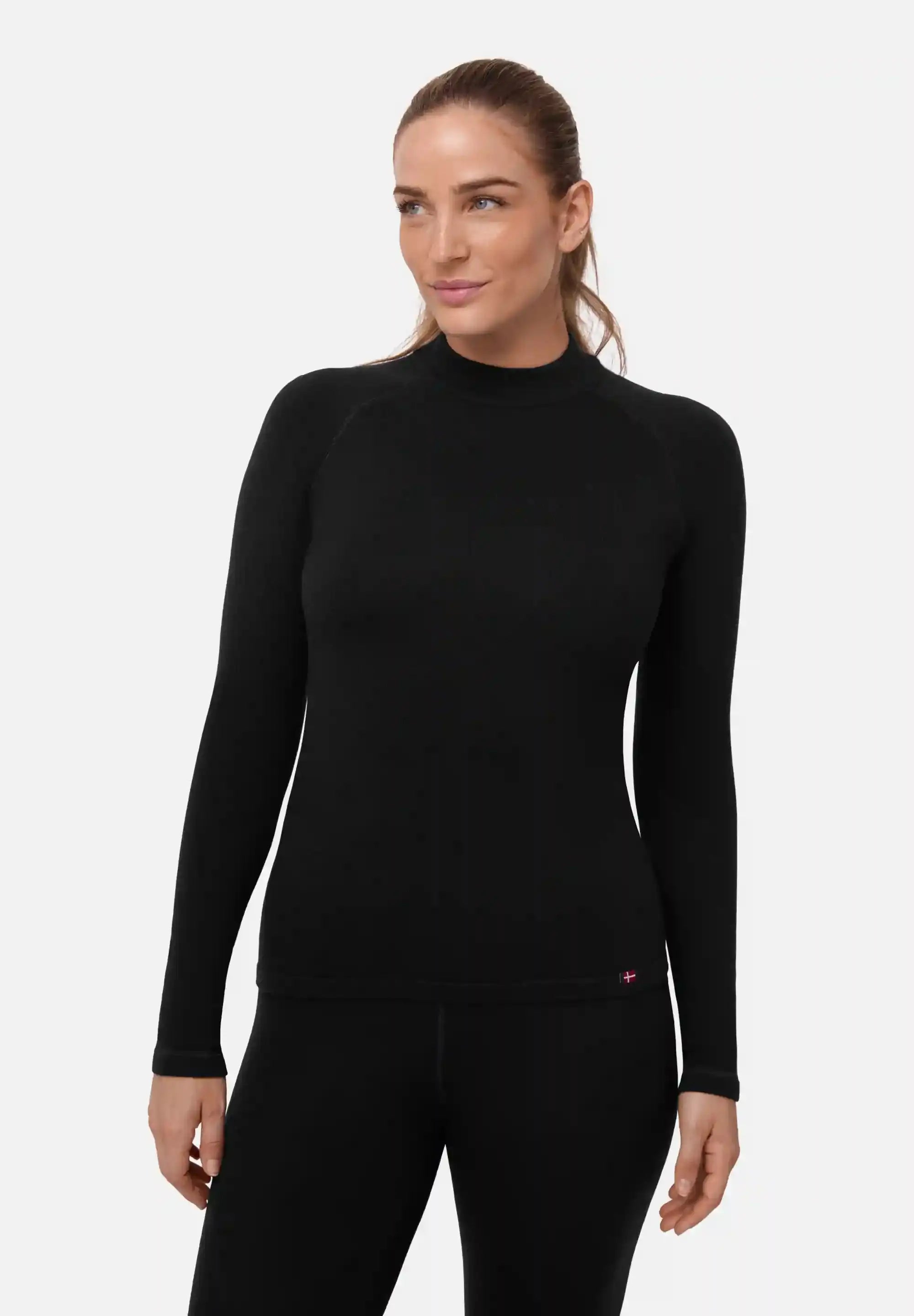 Woman wearing a black, long-sleeve merino base layer shirt, hair tied back, looking to the side.