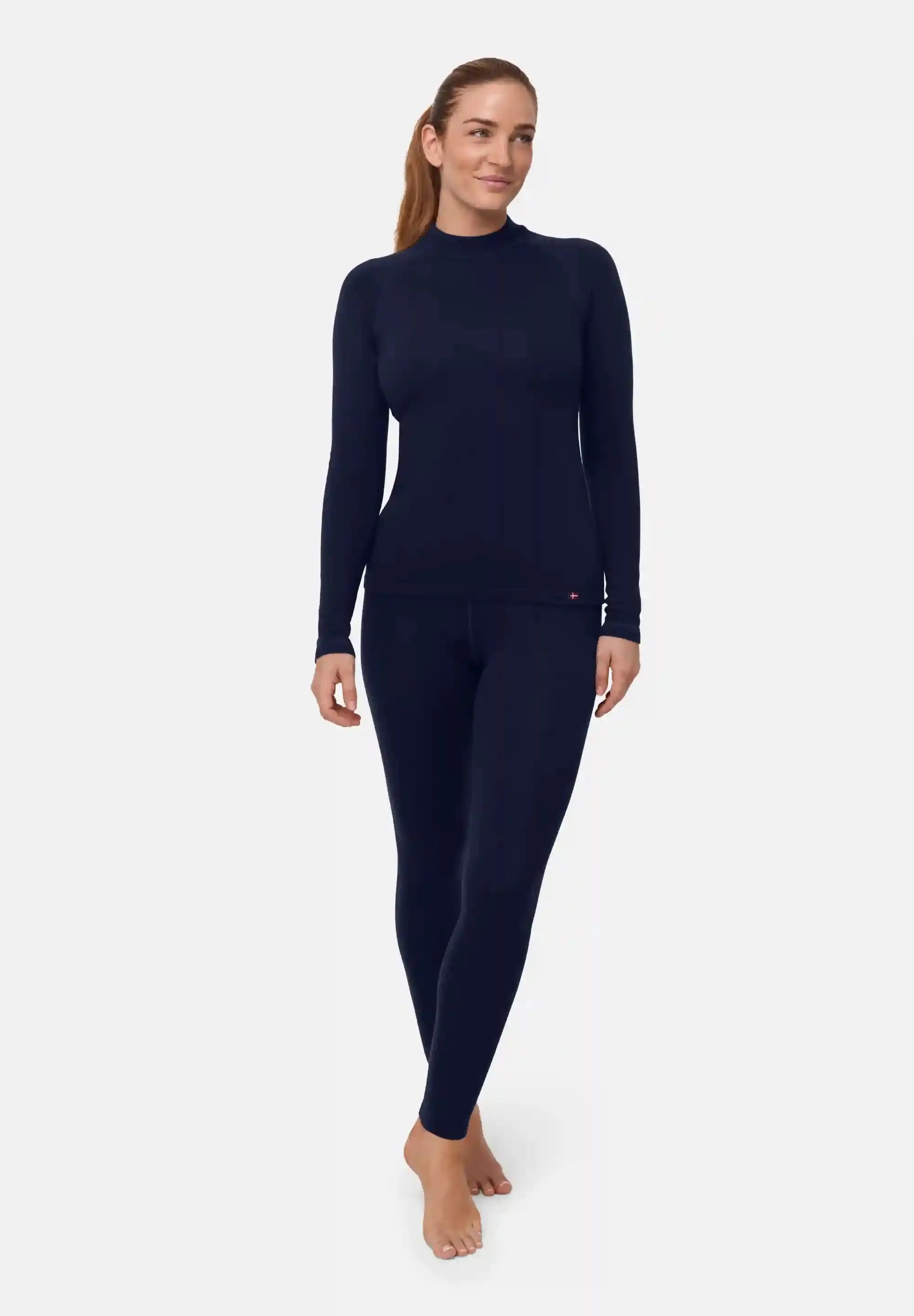 Woman in dark blue merino base layer set, long-sleeve top and leggings, standing barefoot.