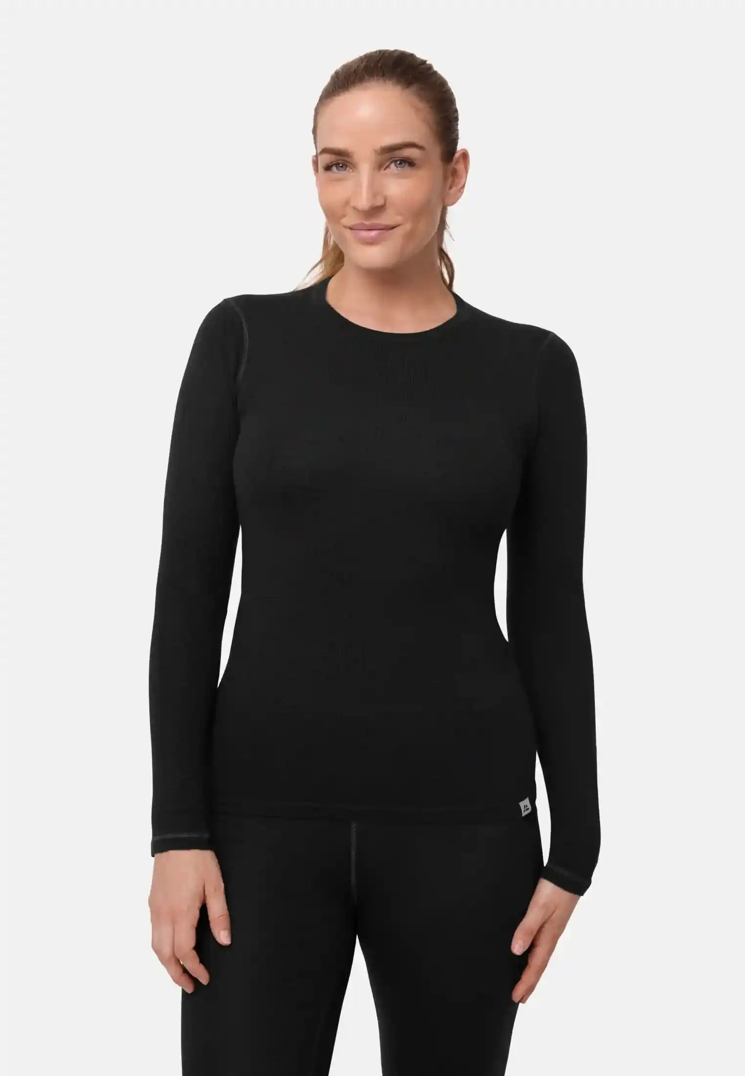 Woman wearing a black, long-sleeved merino wool base layer shirt, standing against a plain backdrop.