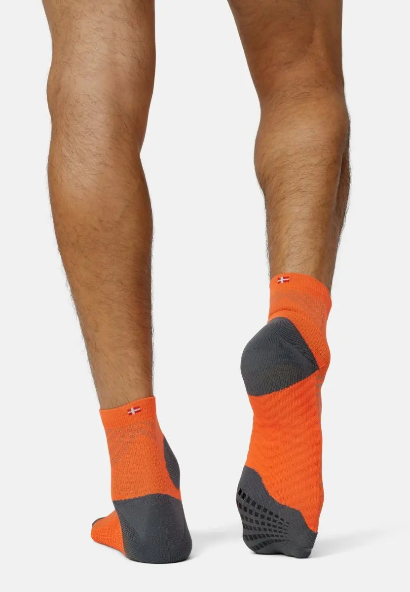 Person wearing bright orange and gray anti-slip running socks, viewed from the back.