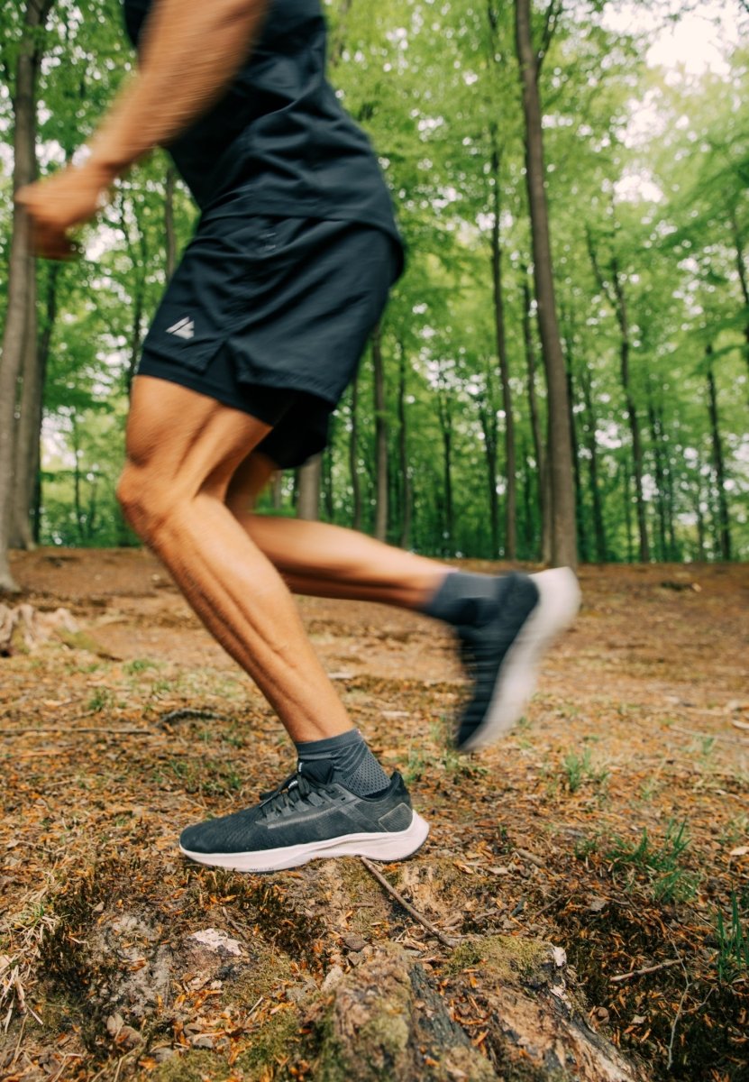 Person running in forest, wearing black anti-slip socks and sneakers, blurred motion.
