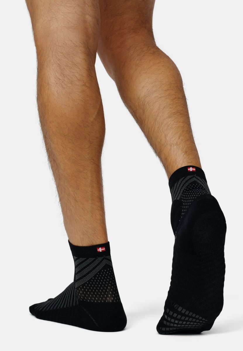 Black running socks with anti-slip soles and flag detail on a person's feet.