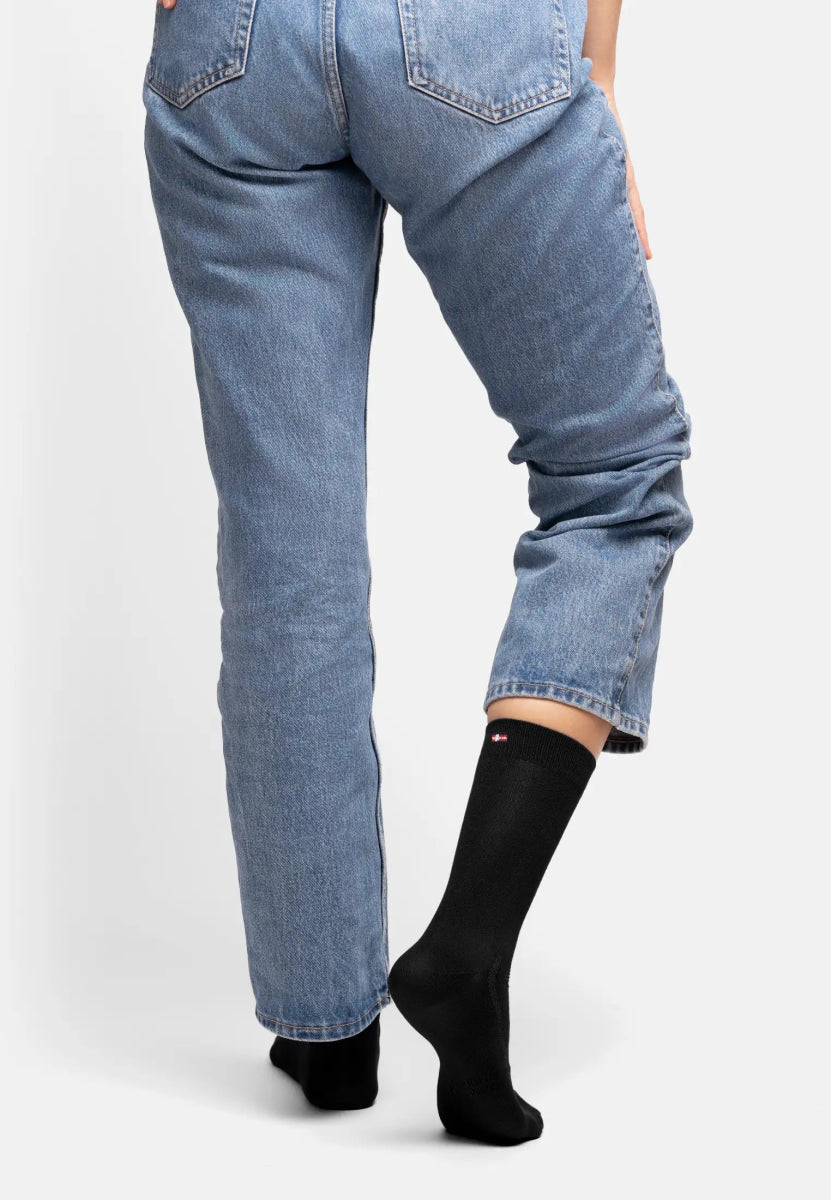Person in blue jeans wearing black bamboo dress socks, one foot raised, showing sock fit.