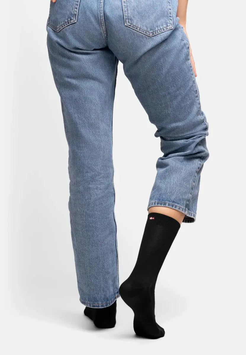 Person in blue jeans wearing black bamboo dress socks, standing on one leg.