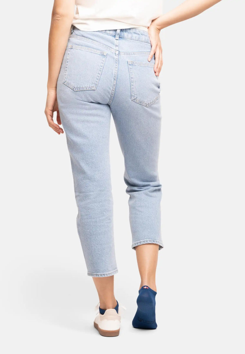 Person in blue jeans and white top wearing one white sneaker and one blue bamboo low-cut sock.