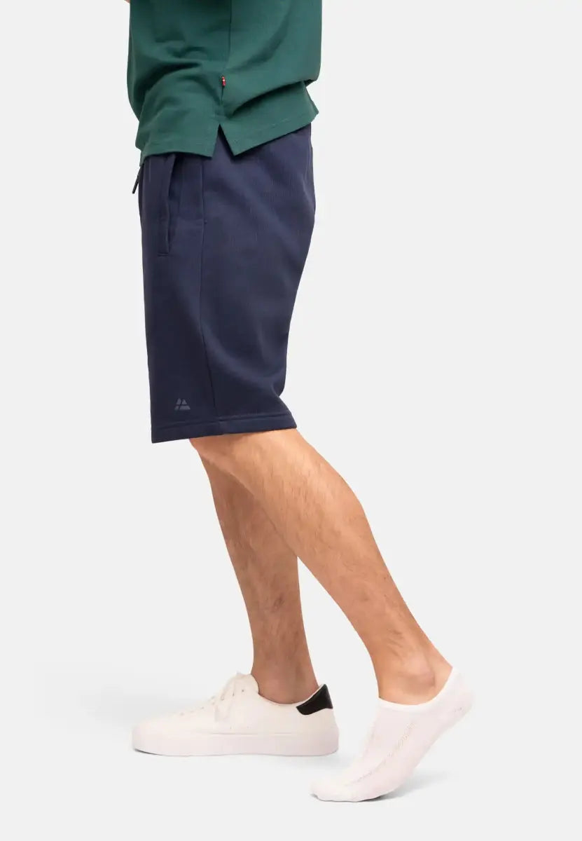 Person wearing navy shorts, green shirt, white no-show socks, and white sneakers with black detail.