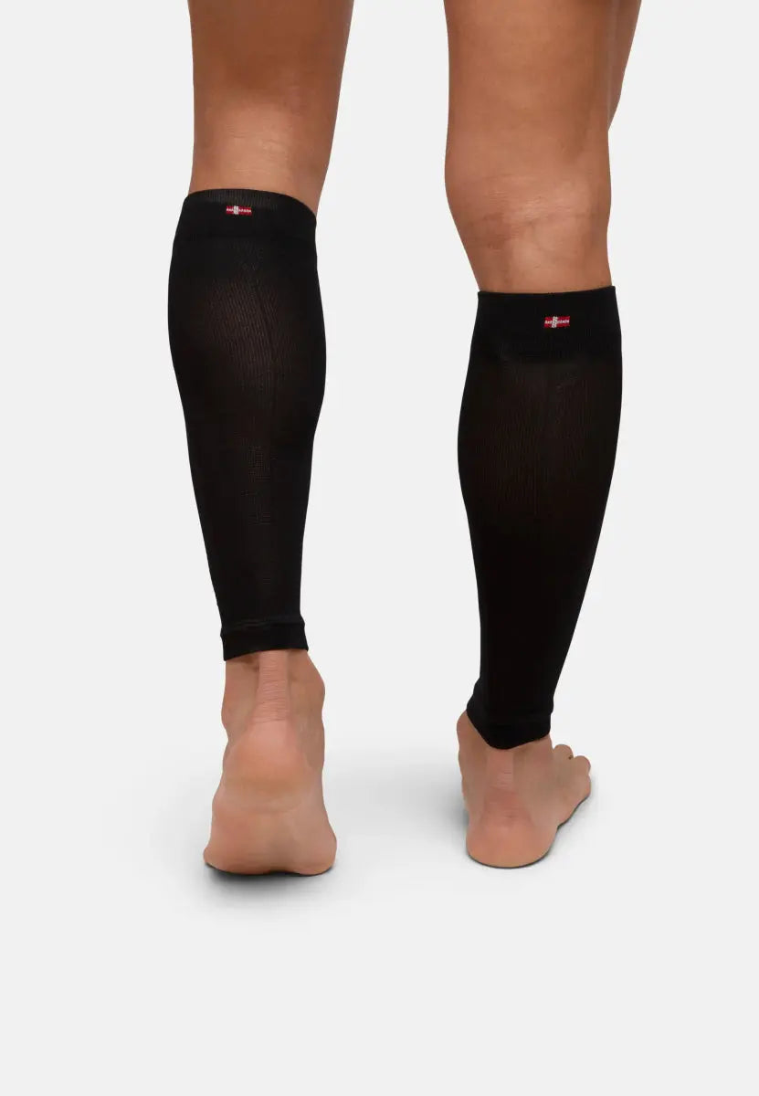 Back view of legs wearing black calf compression sleeves, barefoot, on a plain background.