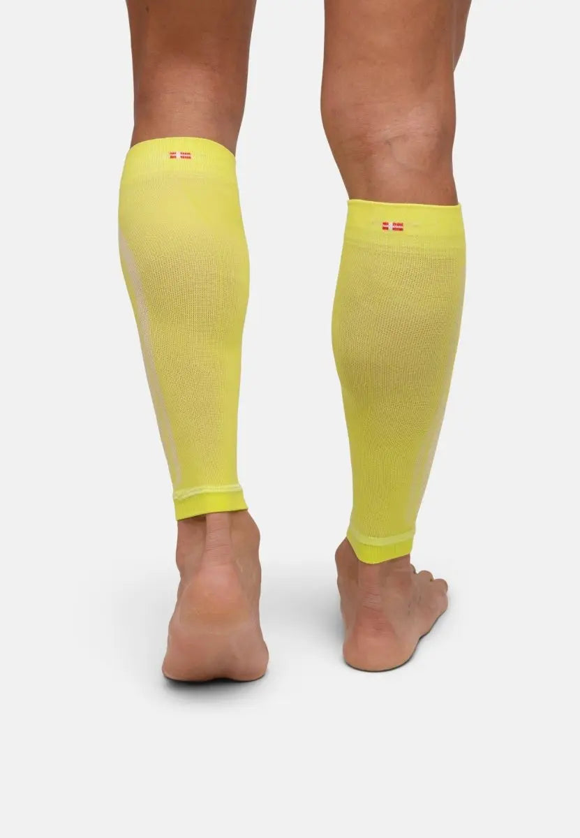 Back view of yellow calf compression sleeves on bare legs, featuring a small flag design near the top.