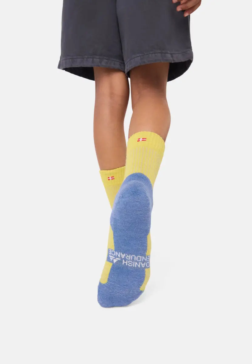 Child wearing yellow and blue merino wool socks with flag design and text on the sole.
