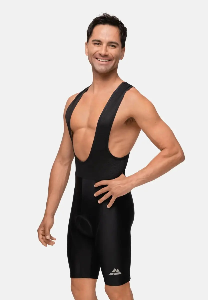 Man wearing black cycling bib shorts, smiling confidently with hands on hips against a plain backdrop.