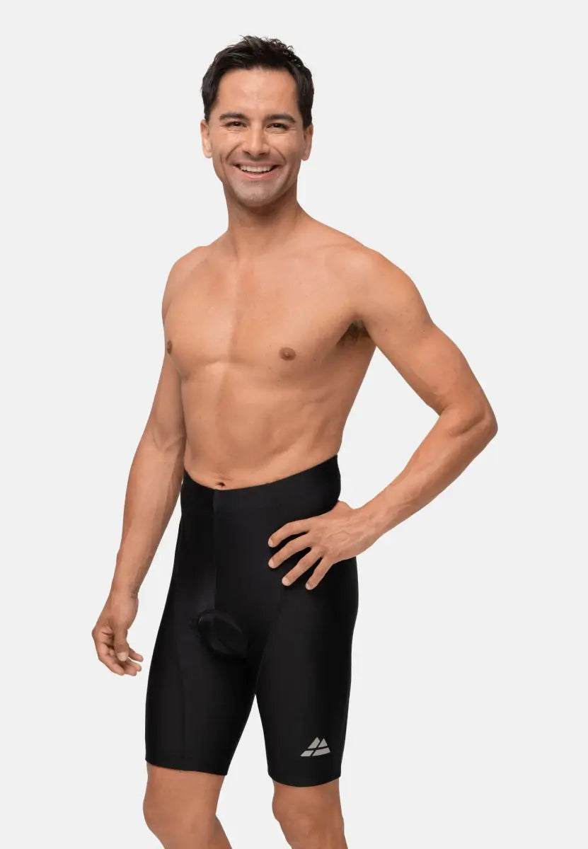 Man wearing black padded bike shorts, smiling confidently, hands on hips, against plain background.