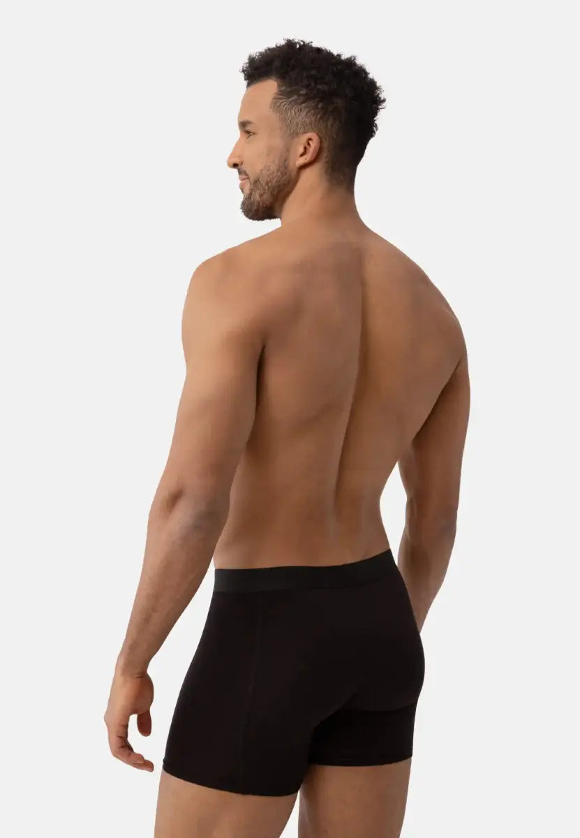 Man wearing black trunks, viewed from the back, showcasing fit and waistband against a light background.