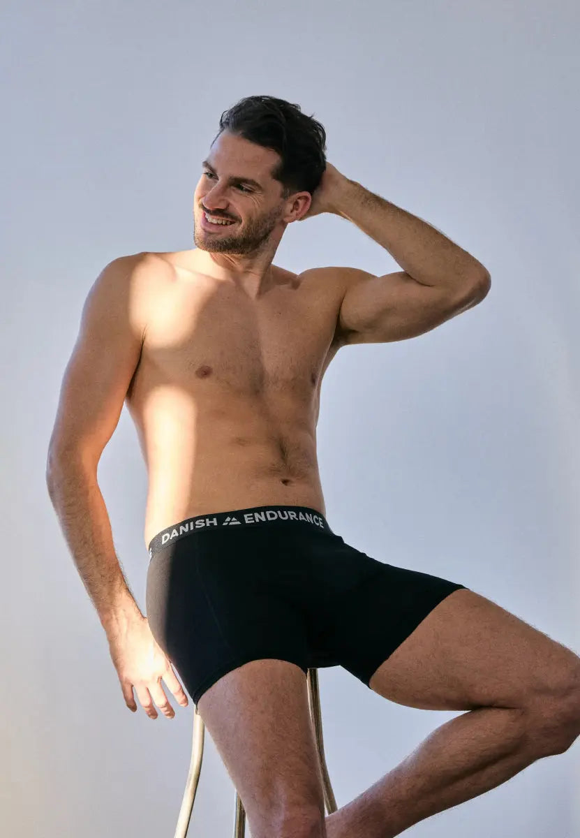 Man sitting on a stool, smiling, wearing black "DANISH ENDURANCE" boxer briefs.