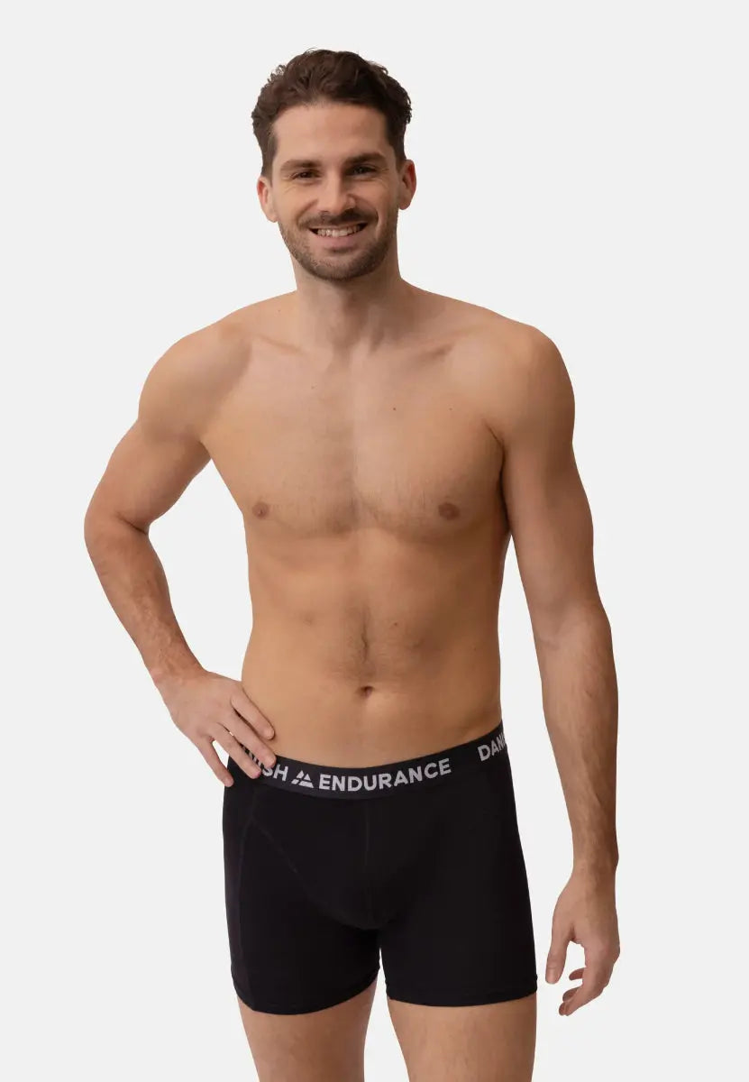 Male model wearing black trunks with "DANISH ENDURANCE" waistband, hand on hip, smiling.