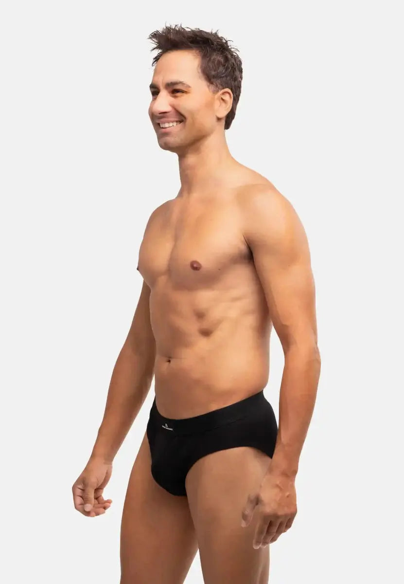 Man in black cotton briefs, standing sideways against a plain white background, smiling.