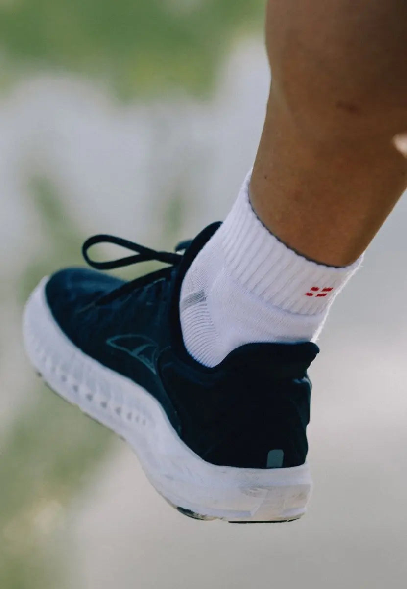 A leg wearing white cotton quarter socks with red detail and a black athletic shoe, blurred background.