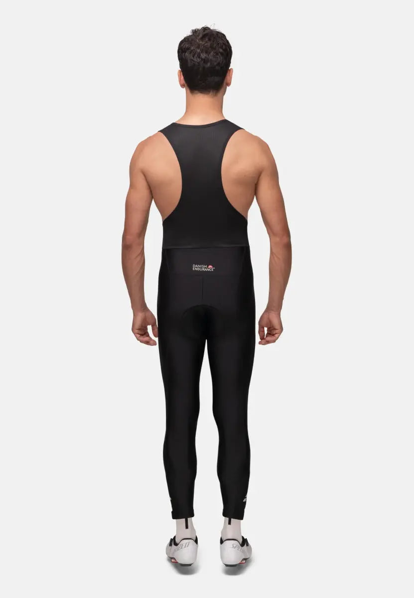 Man wearing black cycling bib pants with racerback, standing, facing away.