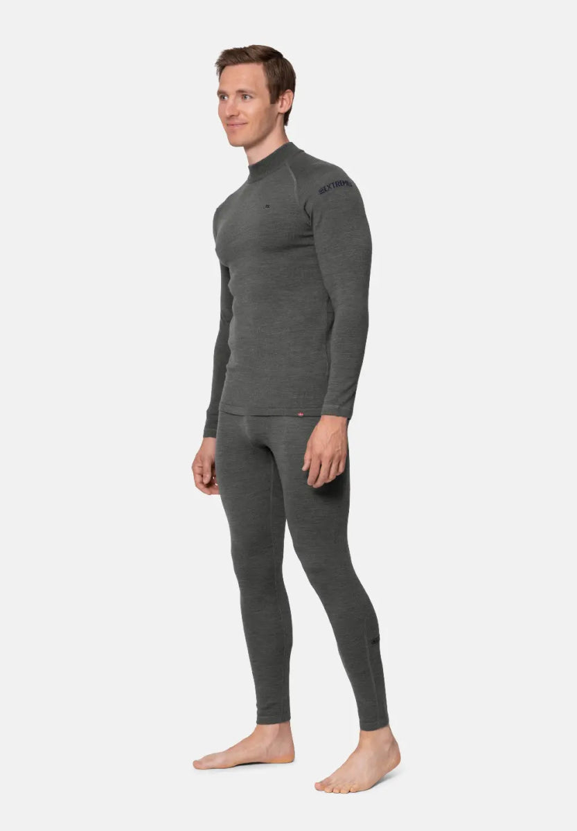 Man in dark grey merino wool base layer set, long-sleeve top and leggings, standing barefoot.