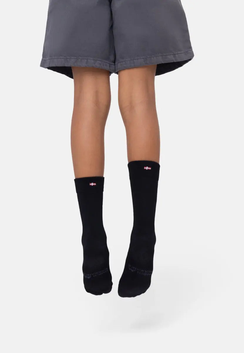 Child wearing knee-length black bamboo socks with a red and white logo near the top, against a white background.