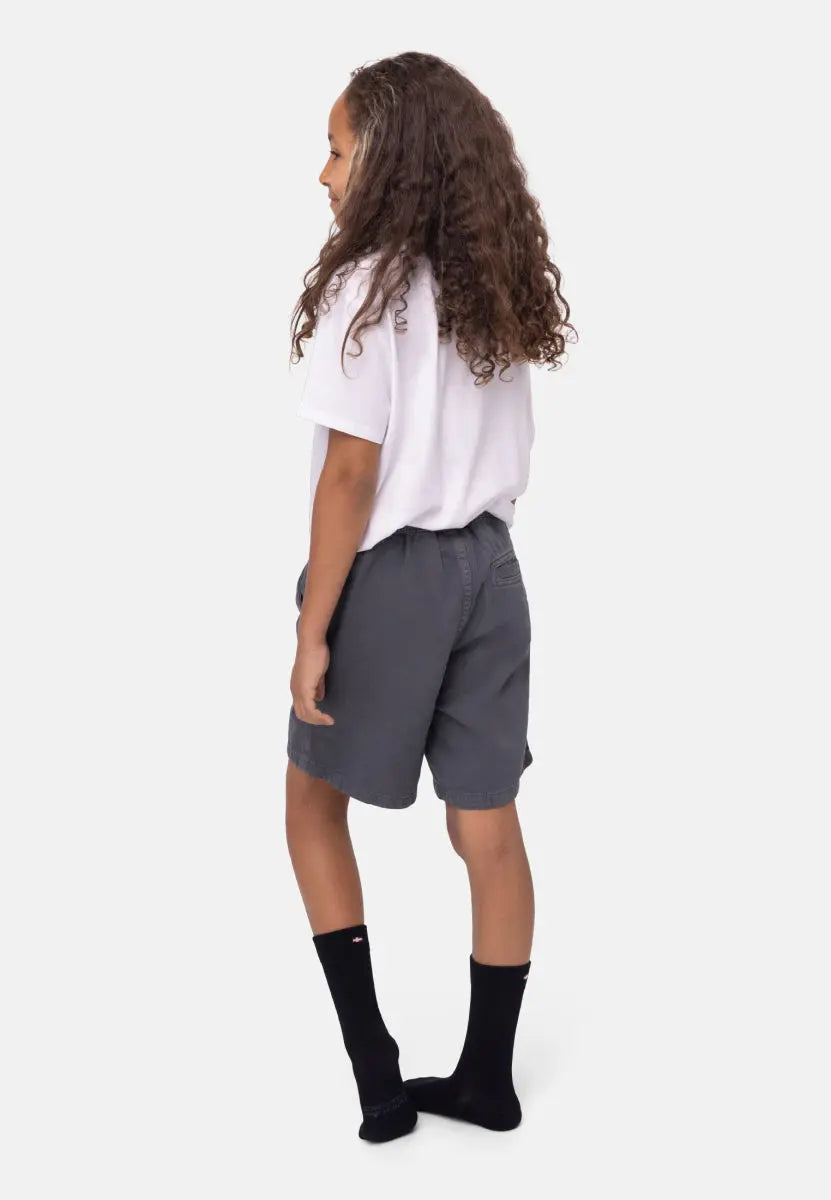 Child in white shirt, gray shorts, black socks, standing sideways against a plain background.