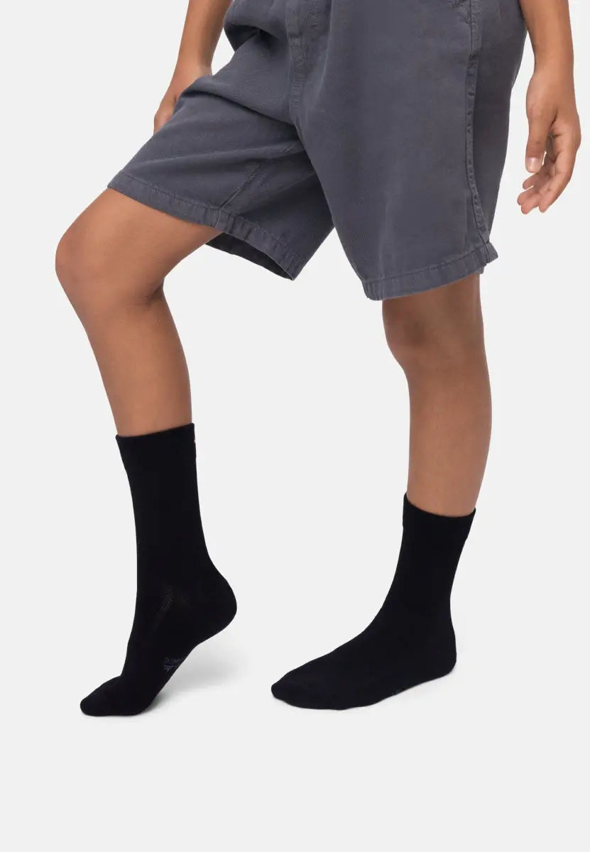 Child wearing black bamboo dress socks with gray shorts, showcasing the socks' fit and style.
