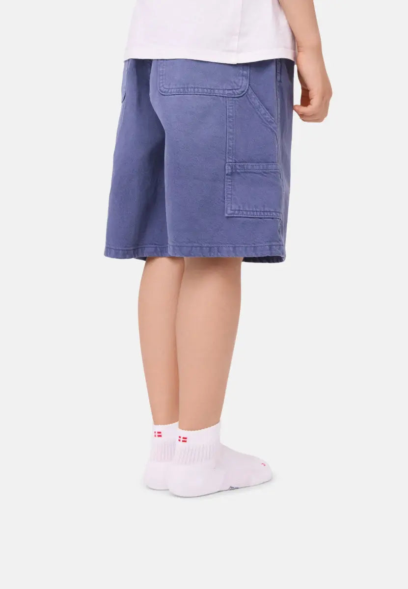 Child in blue shorts wearing white socks with red details, standing on a white background.