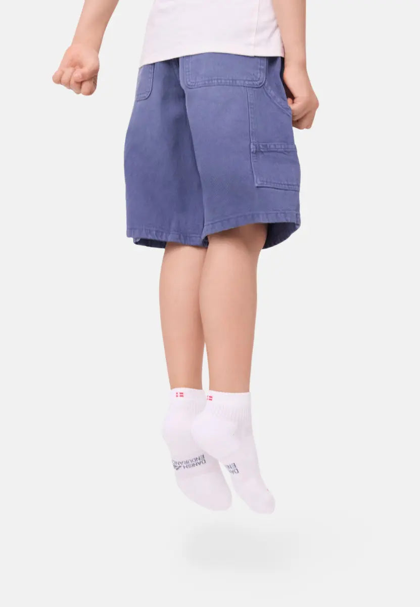 Child jumping in white socks with red detail, wearing blue shorts and a white shirt.