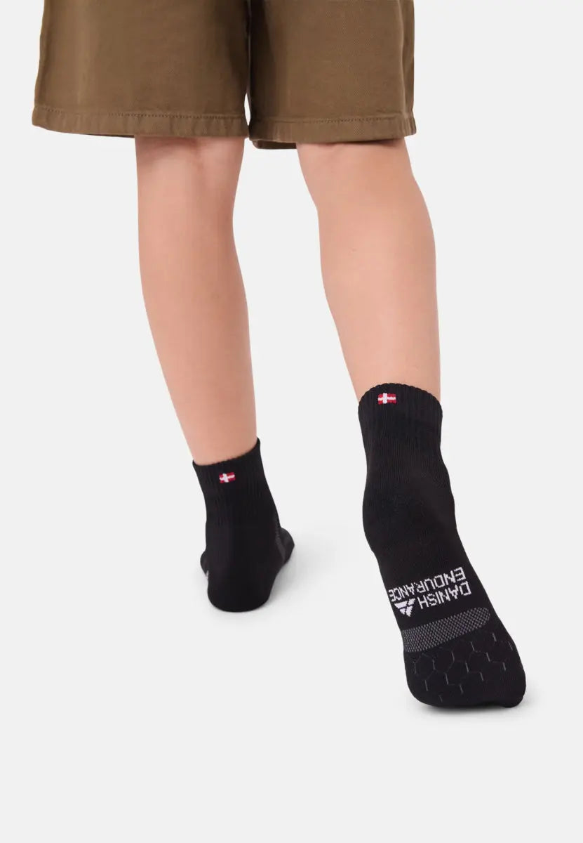 Child wearing black running socks with padding and logo, walking in brown shorts on a light background.