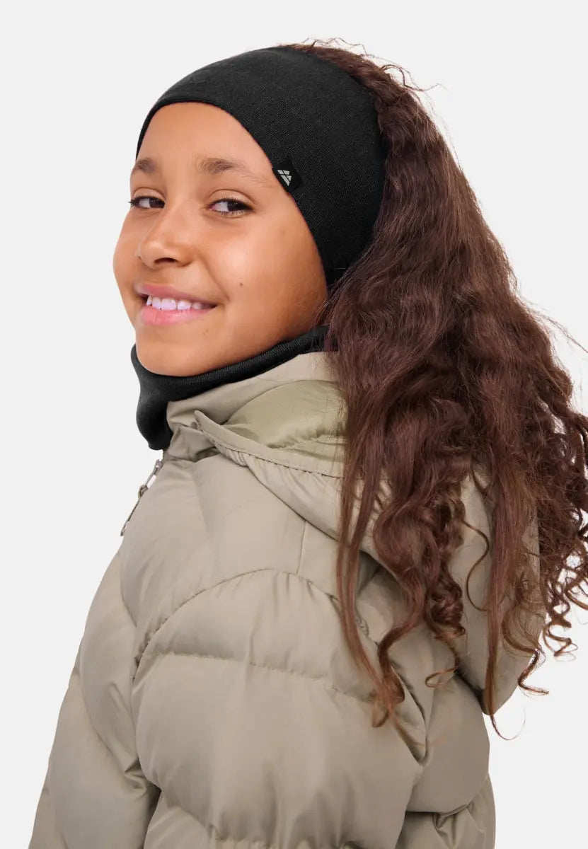 Child in black merino headband and beige puffer jacket, smiling with long curly hair.