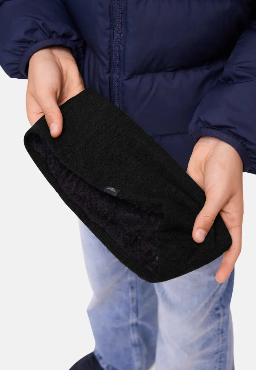 Child in navy jacket holding a black headband with soft fleece lining, wearing light jeans.