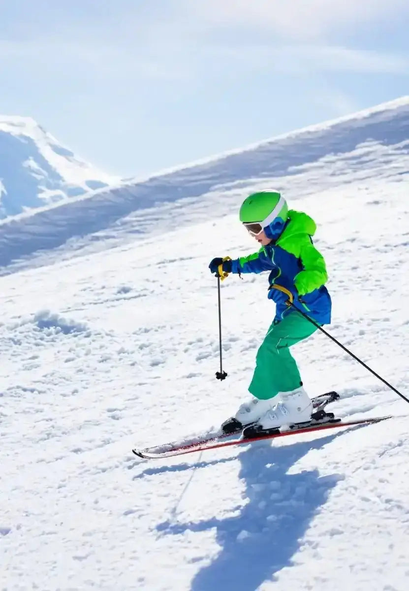 Child skiing downhill in bright green and blue gear, holding poles, on a snowy slope.