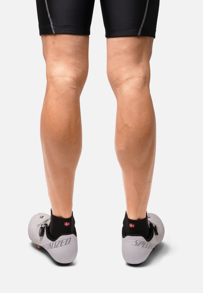 Back view of legs in black low-cut cycling socks, black shorts, and white cycling shoes.