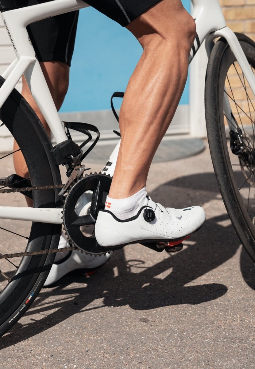 Cyclist on a bike wearing white low-cut socks and white cycling shoes with a black stripe.
