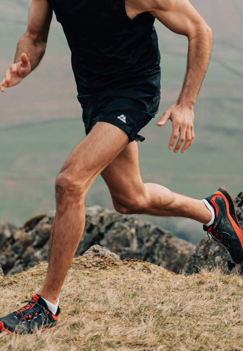 Person running on rocky terrain, wearing low-cut socks and black running shoes with red details.