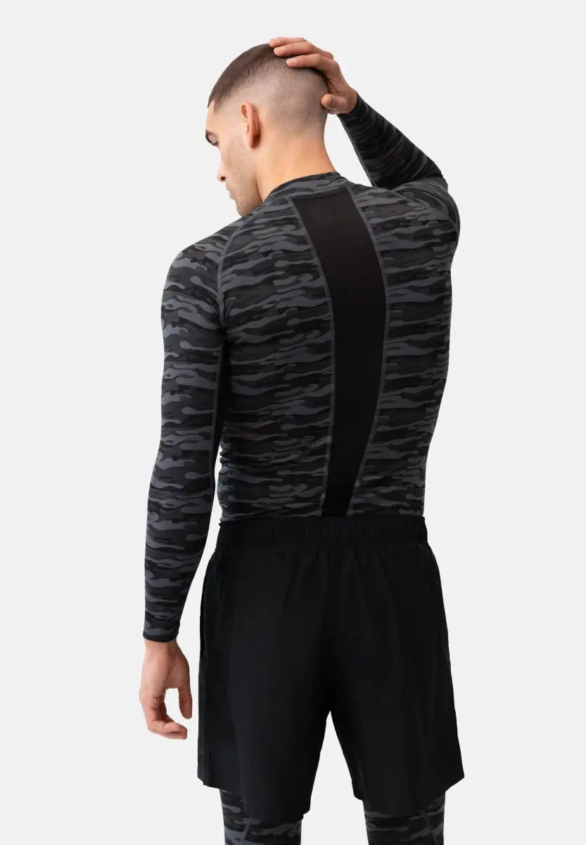 Man in camo long sleeve compression shirt and black shorts, hand on head, viewed from the back.