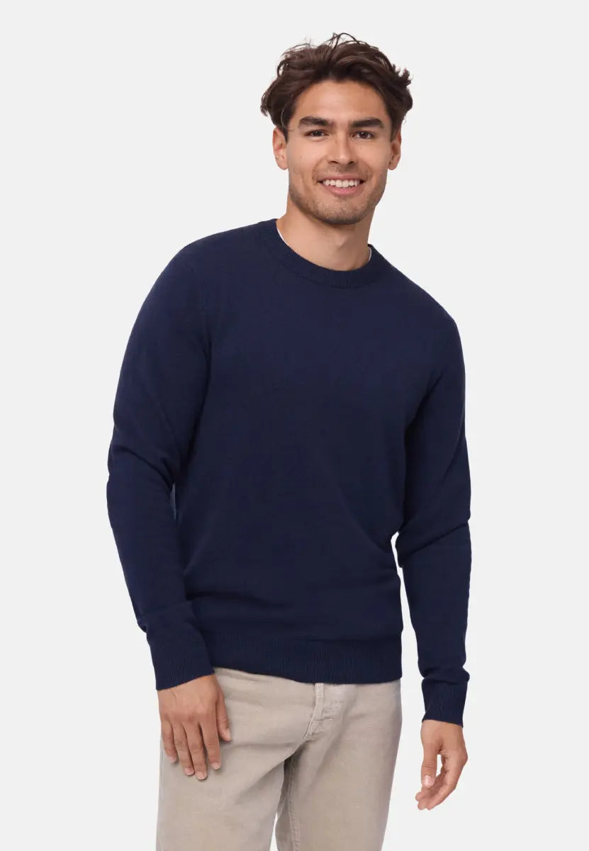 Man in navy merino cashmere sweater and beige pants, smiling against a plain background.
