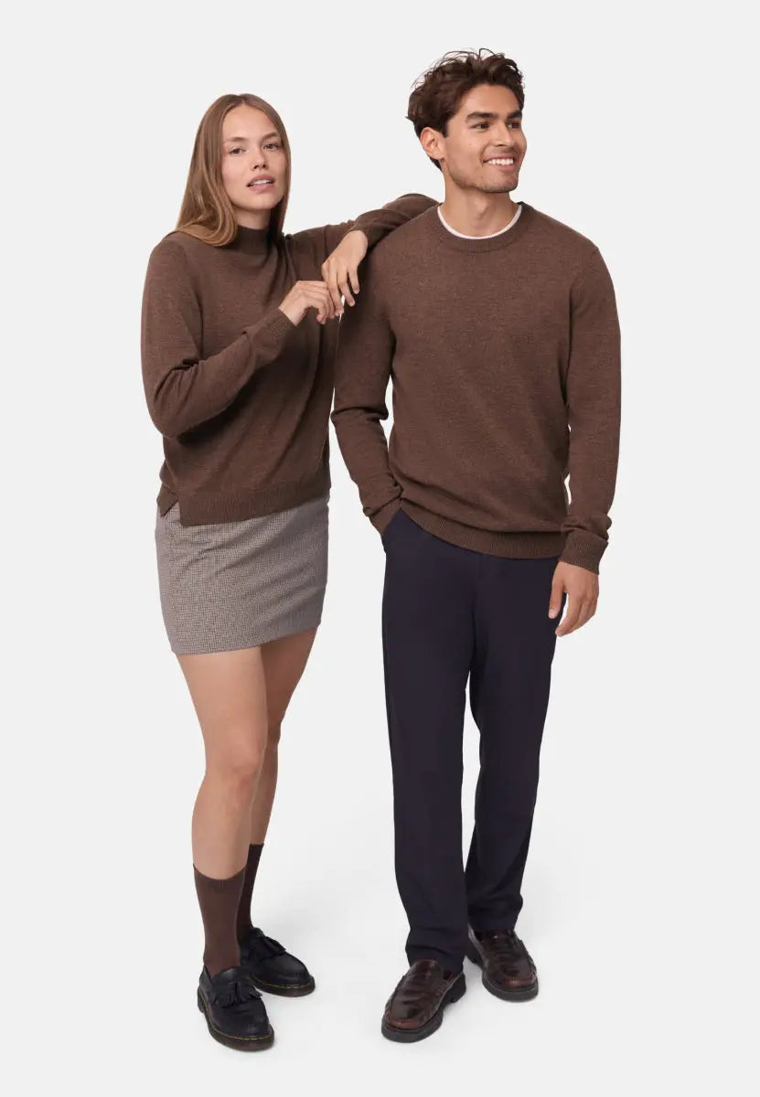 Two people in brown sweaters; man in dark pants, woman in a skirt, standing together smiling.