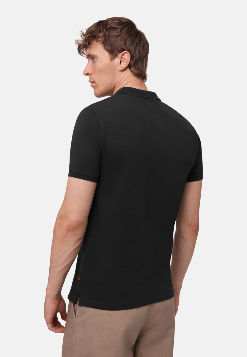 Man wearing a black organic cotton polo shirt, viewed from the back, paired with beige pants.