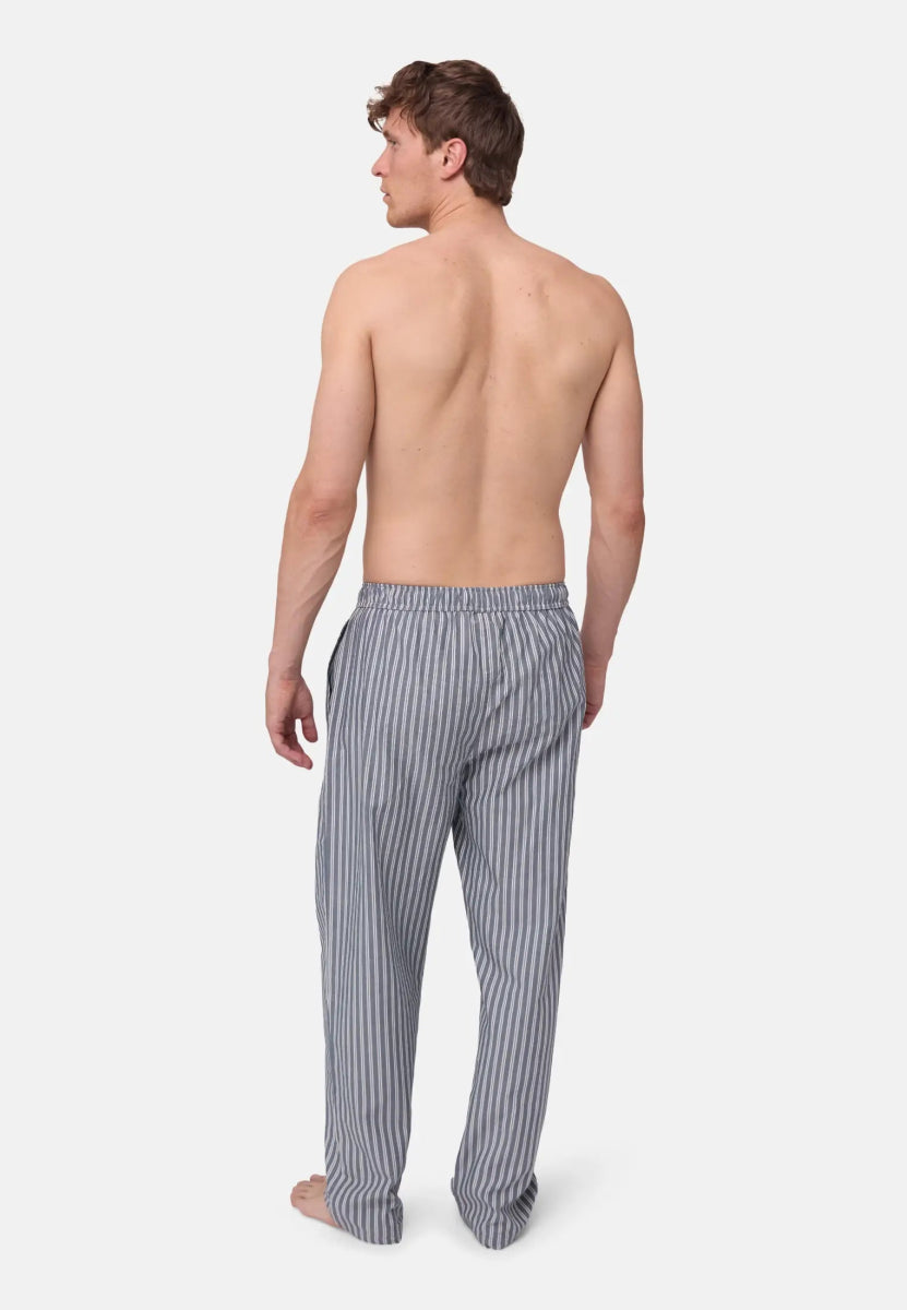 Rear view of a person wearing blue and white striped pyjama pants, standing barefoot.