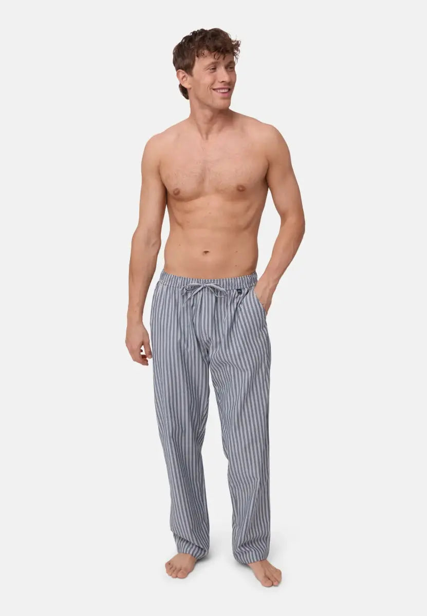 Bare-chested person in striped pajama pants, standing barefoot with hands in pockets.