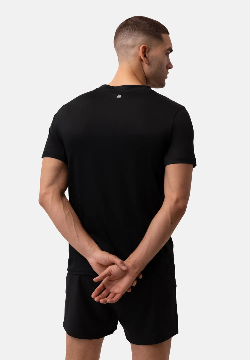 Man in black T-shirt and shorts, viewed from behind with hands clasped.