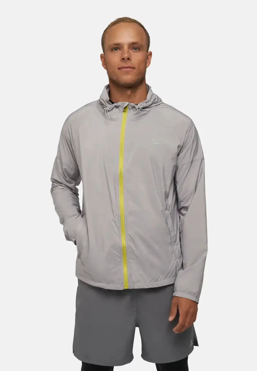 Man wearing a light gray windbreaker with a yellow zipper and matching shorts, hands in pockets.