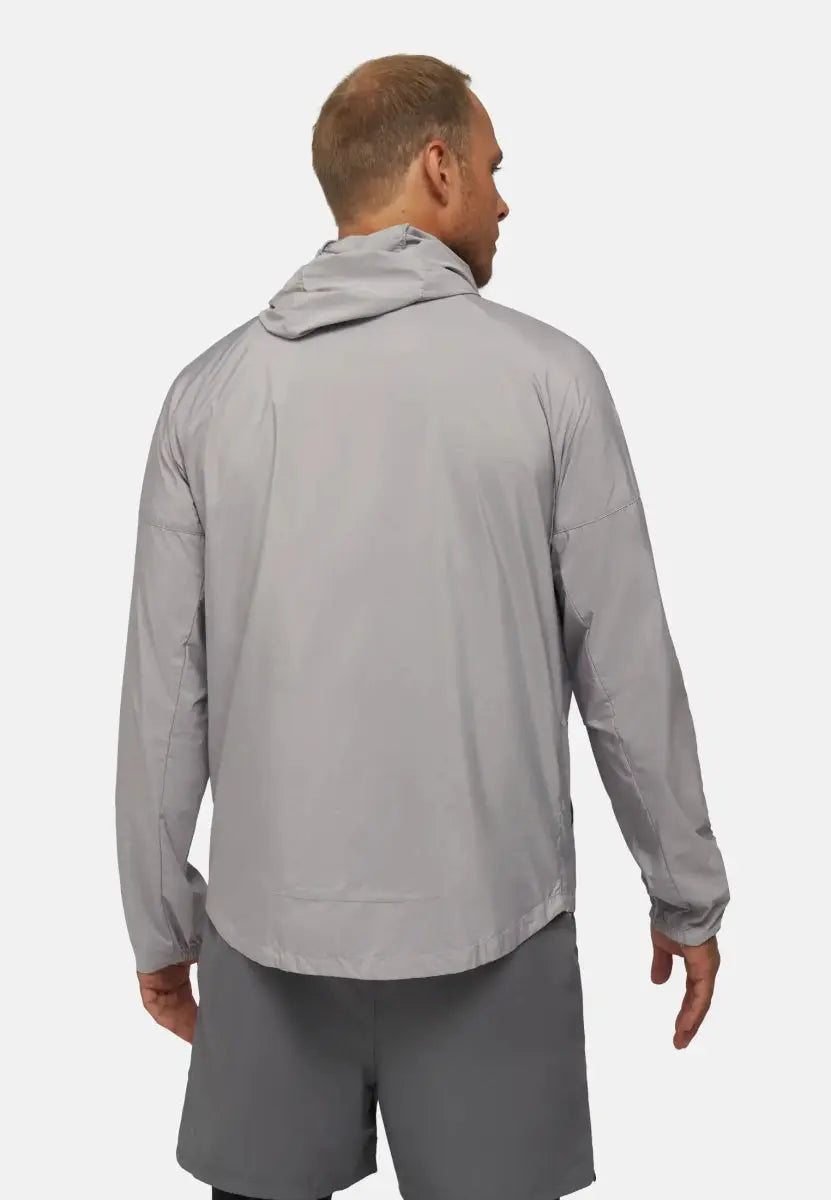 Back view of a person wearing a light gray windbreaker jacket with a hood and dark shorts.