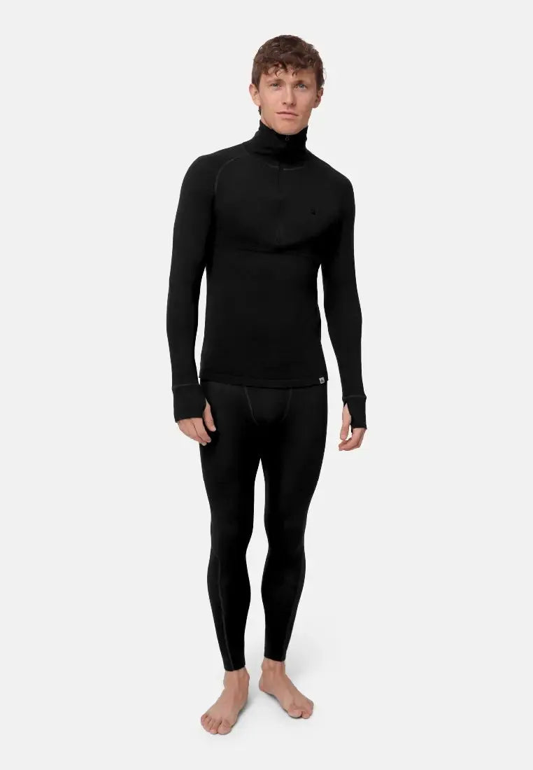 Man in black merino baselayer set with half-zip shirt and leggings, standing barefoot against white.